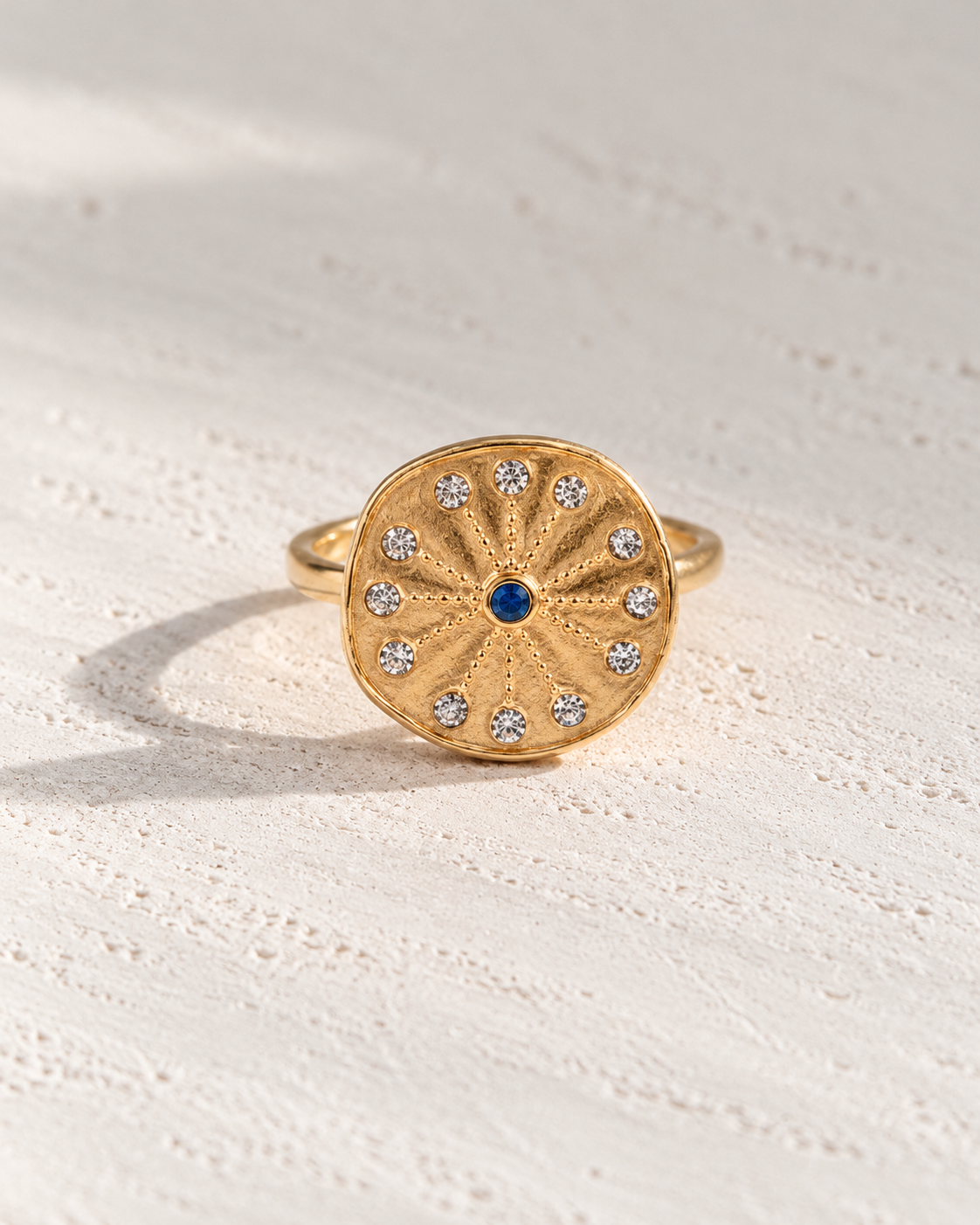 Anillo Zafira medallón dorado con circonitas sobre cemento blanco