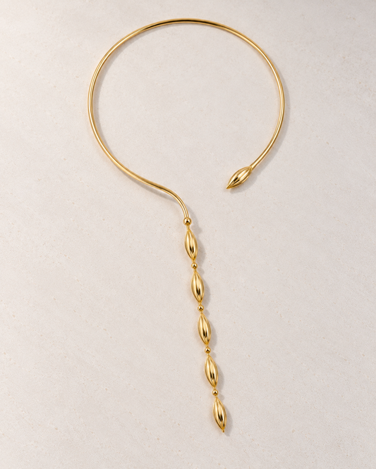 Collar Delphine rígido dorado con cuentas sobre cemento blanco
