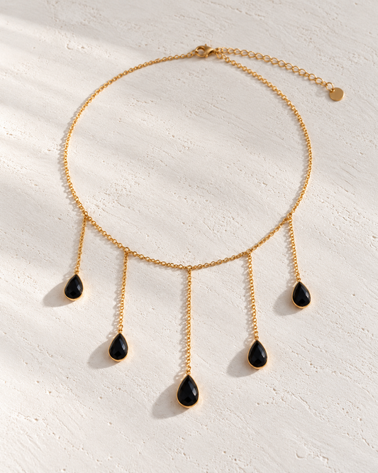 Collar Octavia dorado con lágrimas negras sobre cemento blanco